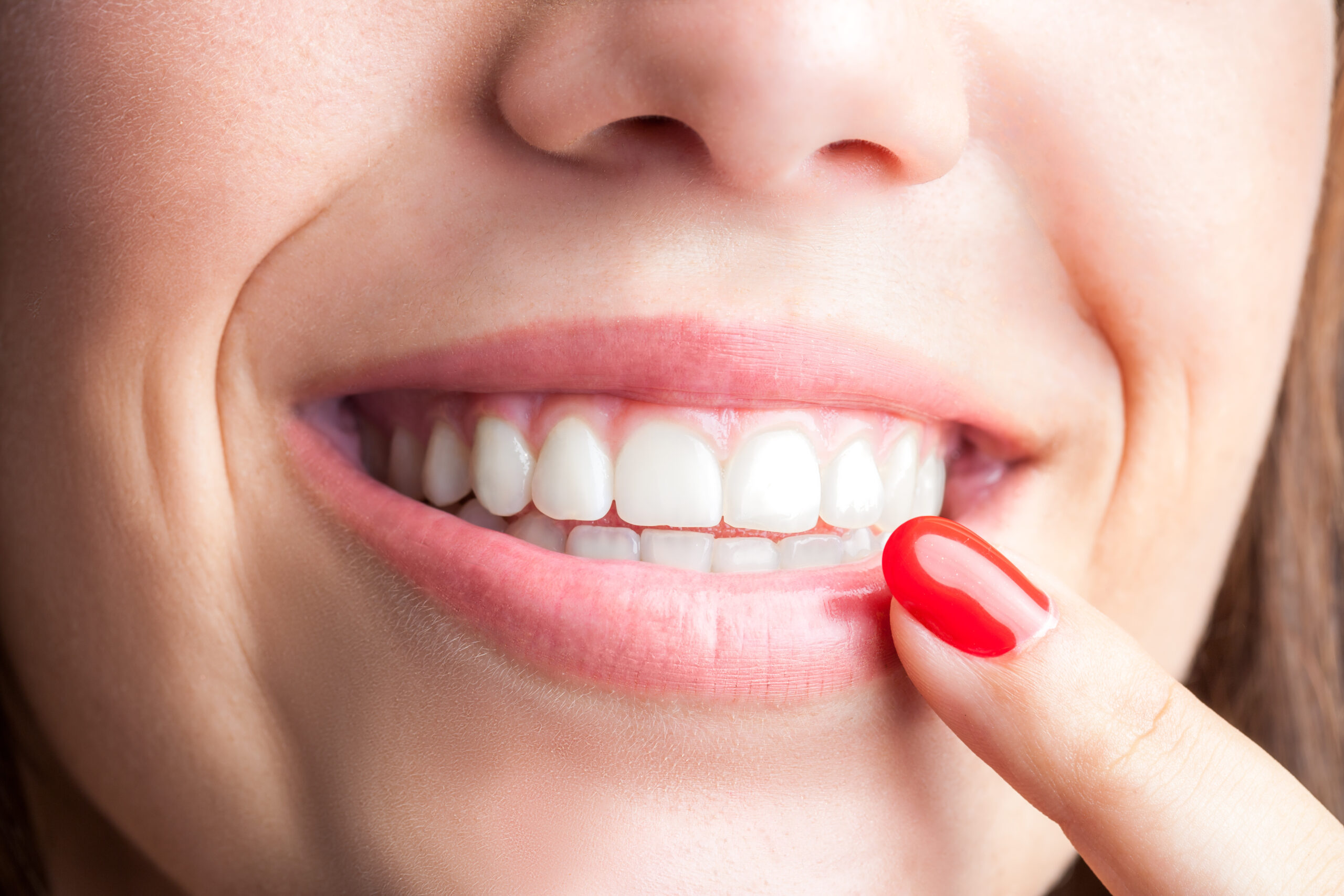 Extreme close up of woman pointing with finger at healthy teeth.